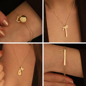 May include: Four gold necklaces and bracelets with charms, including a heart, a dog, a letter 'L', a letter 'A', and a letter 'K'. The charms are on a chain or a bracelet with a bar that says 'Forever' and 'Love is'.