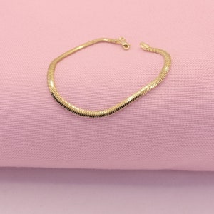 May include: A gold snake chain bracelet on a pink background.