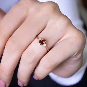 May include: A rose gold ring with a red gemstone and three smaller white gemstones.
