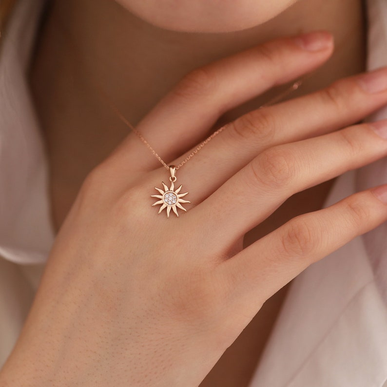 May include: A delicate rose gold necklace with a small sun pendant featuring a clear crystal centre.