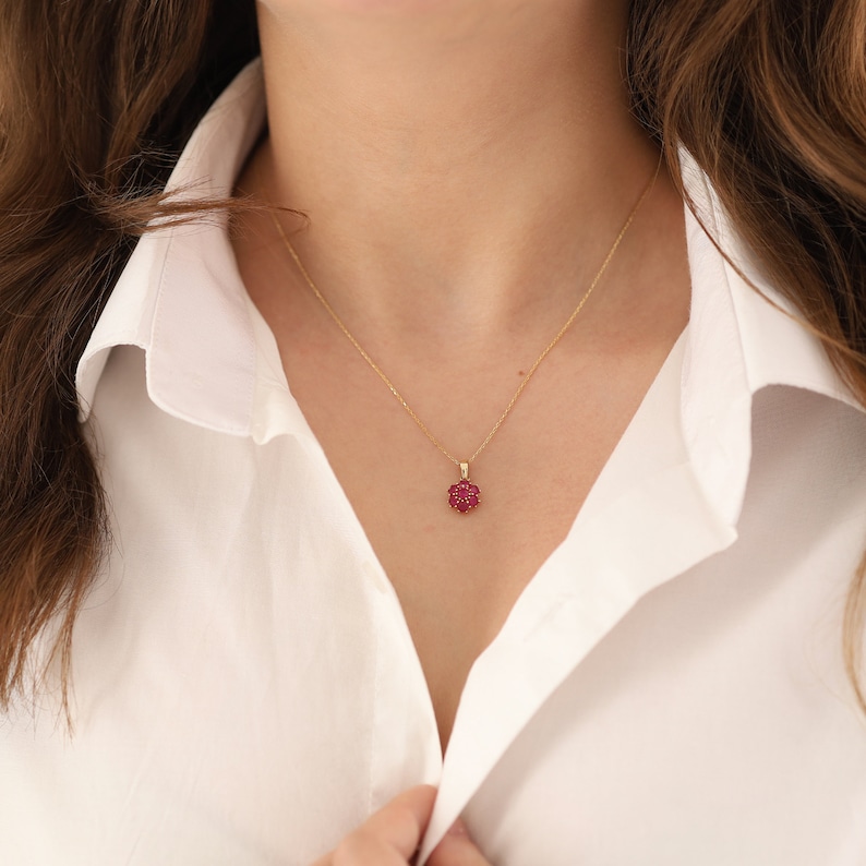May include: A gold chain necklace with a red flower pendant. The pendant is made of small red gemstones set in gold.