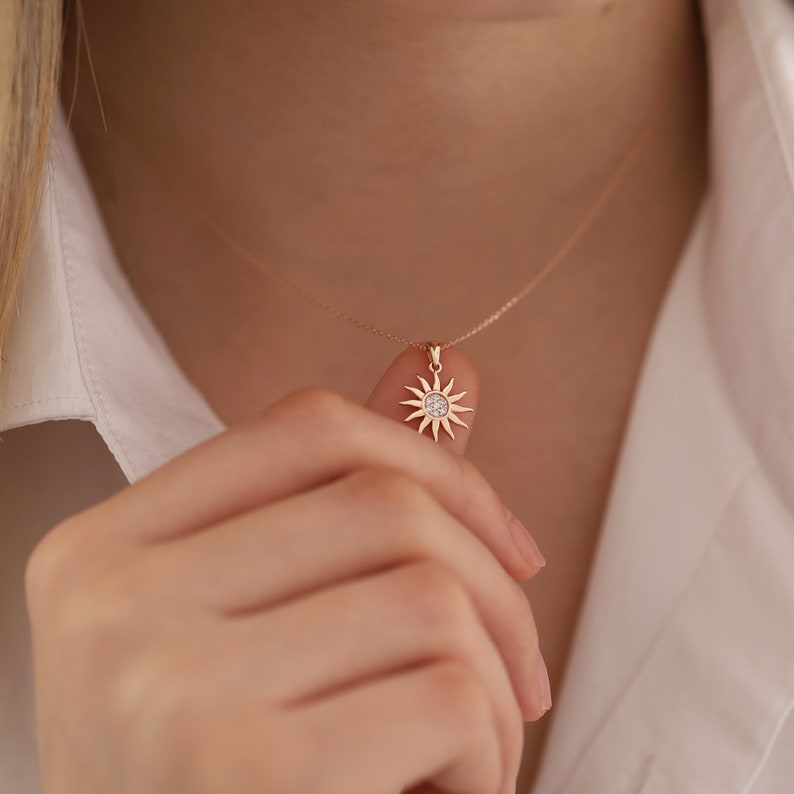 May include: A rose gold necklace with a sun pendant featuring a small round diamond in the centre.