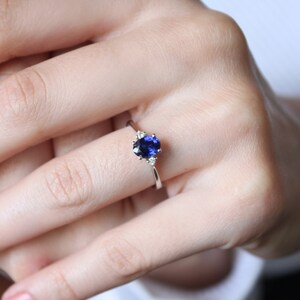 May include: A silver ring with a blue oval sapphire and two smaller diamonds on the band.