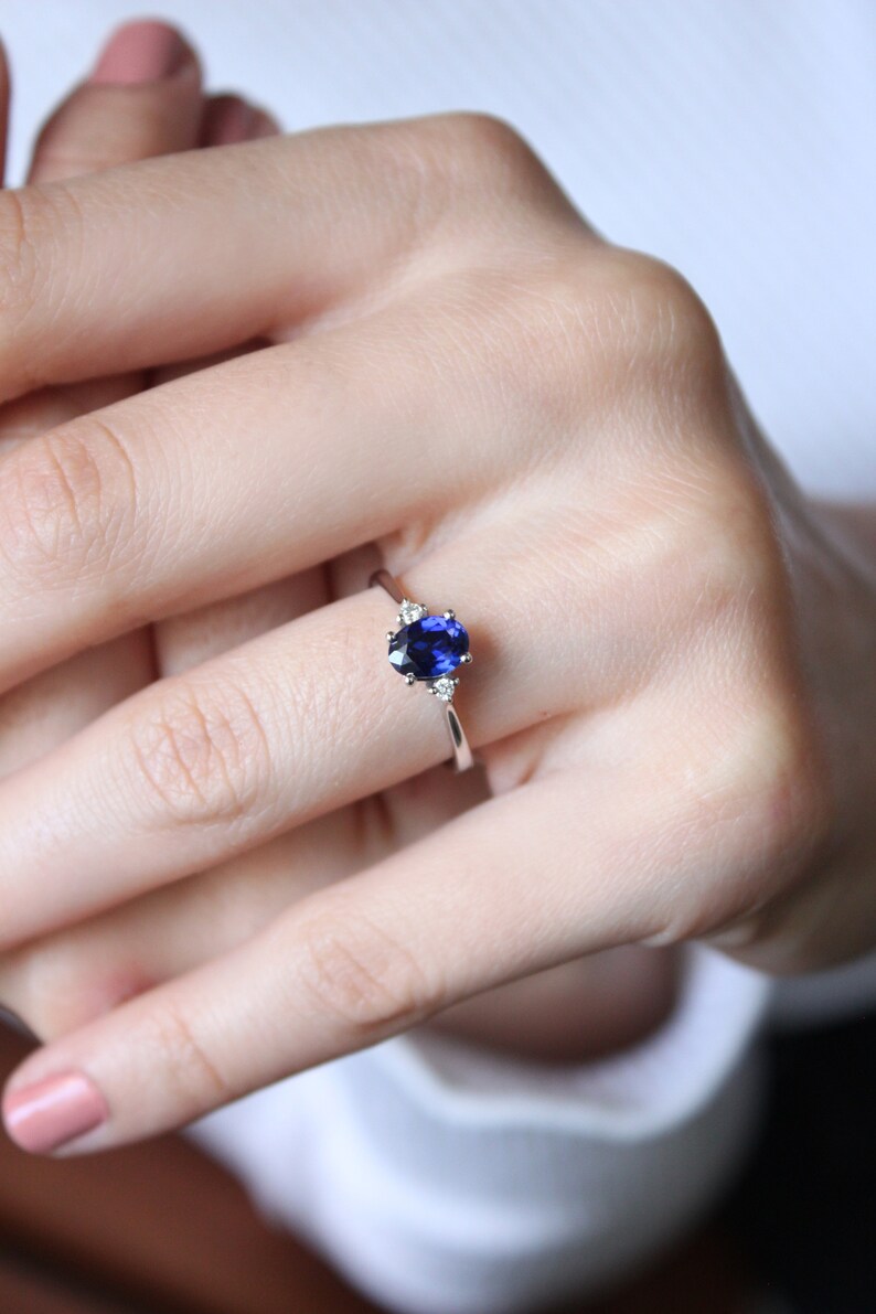 May include: A silver ring with a blue oval sapphire and two smaller diamonds on the band.