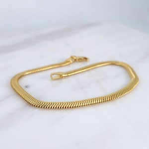 May include: A gold snake chain necklace with a classic design. The chain is made of smooth, polished metal and has a simple, elegant look.