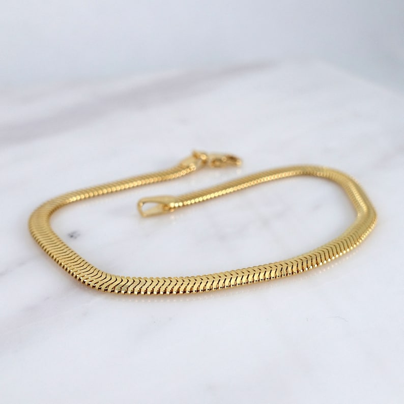 May include: A gold snake chain necklace with a classic design. The chain is made of smooth, polished metal and has a simple, elegant look.