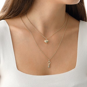 May include: A gold layered necklace with a heart pendant and a key pendant.