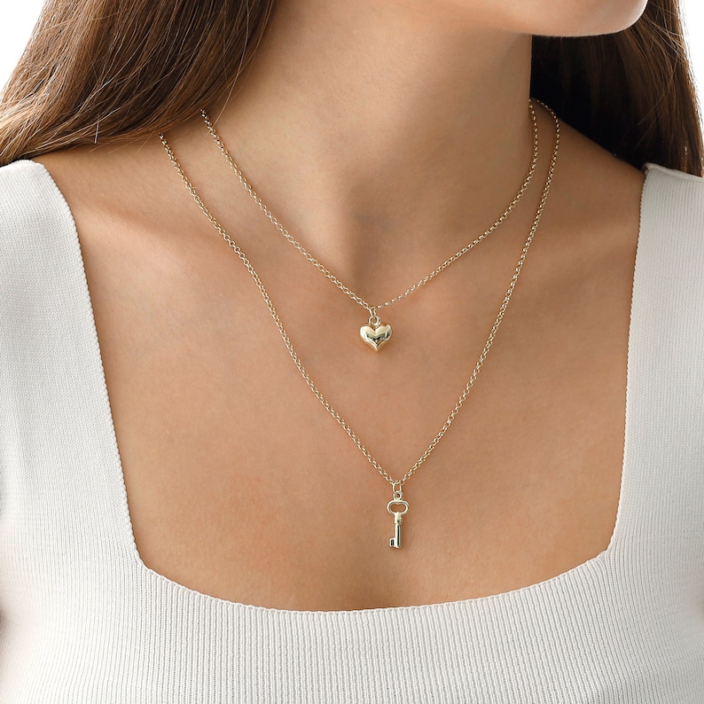 May include: A gold layered necklace with a heart pendant and a key pendant.