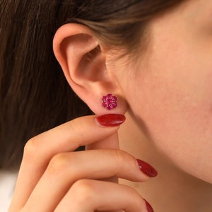 May include: A pair of ruby stud earrings with a flower-shaped design. The earrings are set in gold and feature a cluster of small, red rubies.