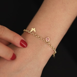 May include: A gold chain bracelet with a pink gemstone and two butterfly charms.