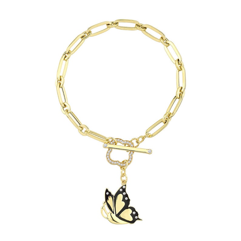 K&ouml;nnte beinhalten: Ein goldenes Kettenarmband mit einem Toggle-Verschluss in Herzform, der mit klaren Steinen besetzt ist. An dem Verschluss h&auml;ngt ein Anh&auml;nger in Form eines schwarzen Schmetterlings mit wei&szlig;en Akzenten.