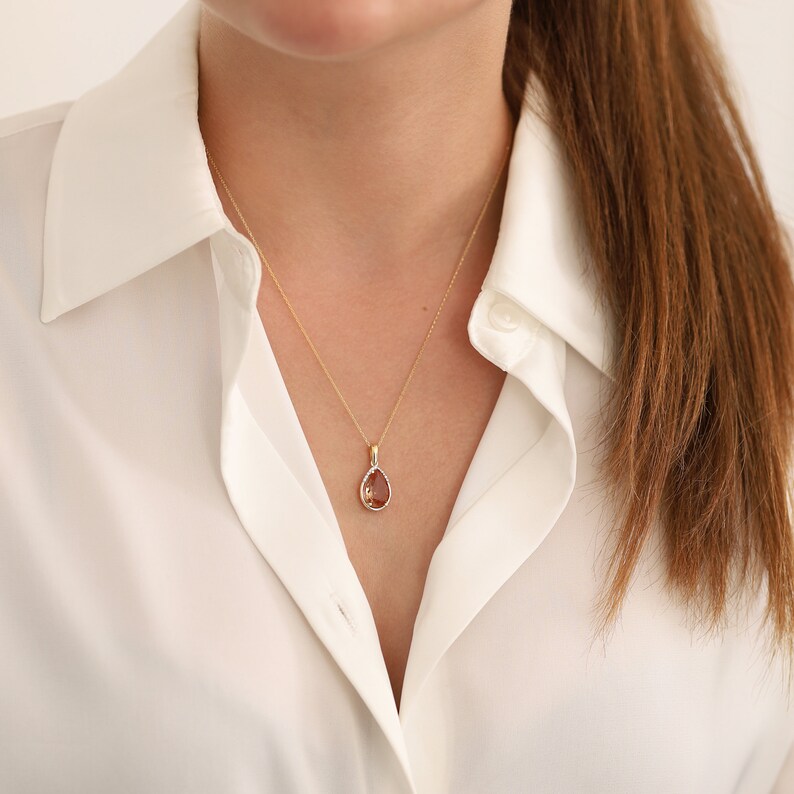Pu&ograve; includere: Una collana con catena d'oro con un ciondolo a forma di lacrima con una pietra preziosa marrone.