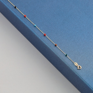 May include: A gold chain necklace with colorful beads. The beads are red, black, blue, and brown.