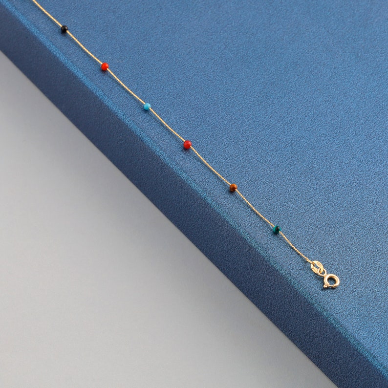 May include: A gold chain necklace with colorful beads. The beads are red, black, blue, and brown.