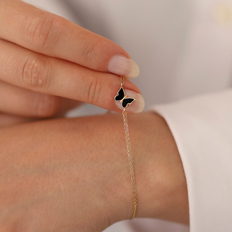 May include: A delicate gold chain bracelet with a black enamel butterfly charm.