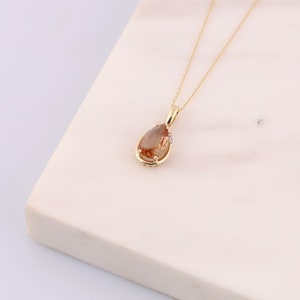 Pu&ograve; includere: Una collana d'oro con un ciondolo a forma di pera in pietra preziosa marrone decorato con piccoli diamanti.