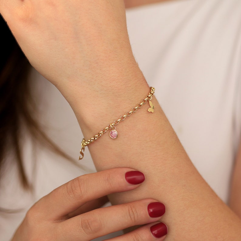 May include: A gold chain bracelet with a pink gemstone charm and a butterfly charm.