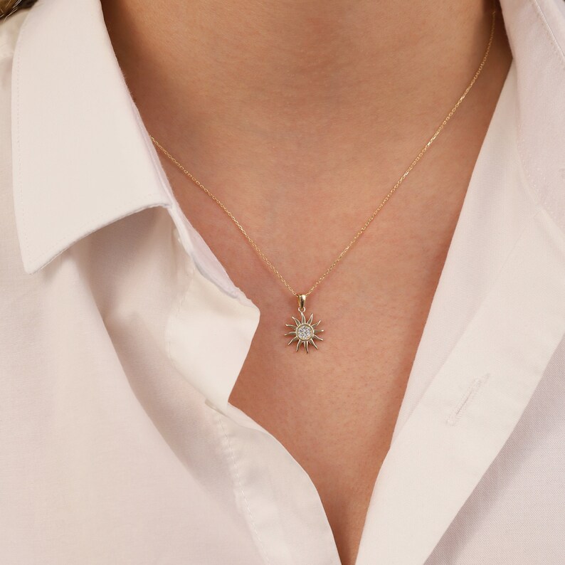 May include: A gold necklace with a small sun pendant featuring a clear crystal in the centre.