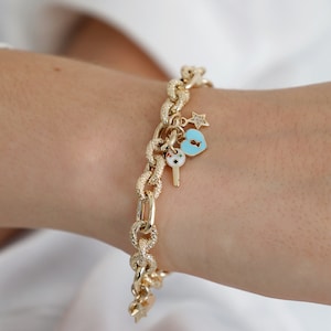 May include: A gold chain bracelet with a textured finish and multiple charms, including a blue heart with a keyhole, a key with a colorful design, and a star.