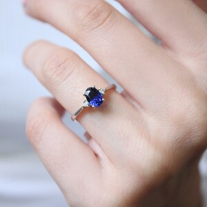 May include: A silver ring with a blue oval gemstone and smaller clear gemstones on the band.