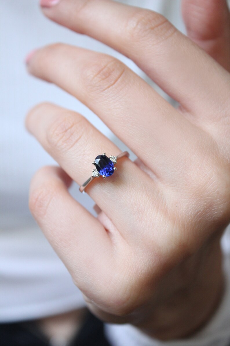 May include: A silver ring with a blue oval gemstone and smaller clear gemstones on the band.