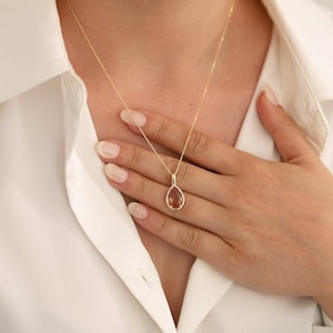 Pu&ograve; includere: Una collana con catena d'oro con un ciondolo a forma di pera con una pietra preziosa marrone circondata da pietre preziose trasparenti pi&ugrave; piccole.