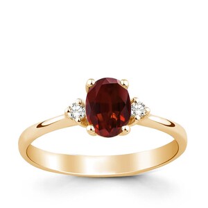 May include: A gold ring with a red oval gemstone and two smaller white gemstones on the sides.