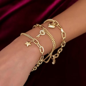 Könnte beinhalten: Ein Set aus vier goldenen Kettenarmbändern mit Anhängern. Die Anhänger sind ein Herz, ein Schlüssel und ein Stern.