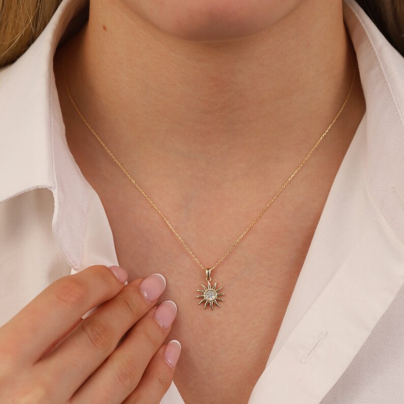 May include: A gold chain necklace with a small sun pendant featuring a clear crystal in the centre.