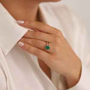 May include: A gold ring with a green oval gemstone. The ring is worn on the ring finger of a hand.