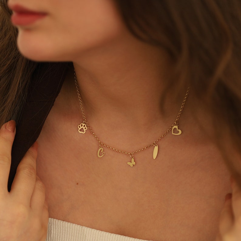 May include: A gold chain necklace with multiple charms, including a paw print, a heart, a letter C, a butterfly, and a long, thin oval charm.
