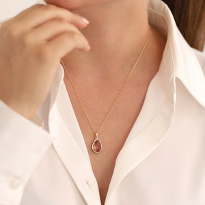 Pu&ograve; includere: Una collana con catena d'oro con un ciondolo a forma di lacrima con una pietra preziosa marrone.