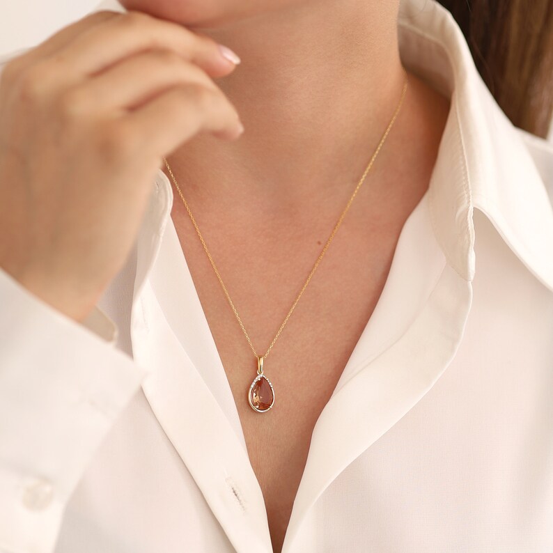 Pu&ograve; includere: Una collana con catena d'oro con un ciondolo a forma di lacrima con una pietra preziosa marrone.