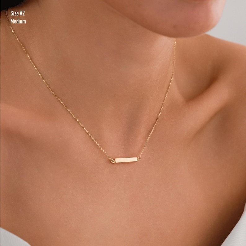 May include: A gold chain necklace with a thin, rectangular pendant. The pendant is a simple, minimalist design.