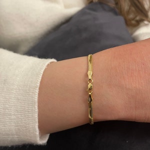 May include: A gold snake chain bracelet with a clasp that has the inscription "925".
