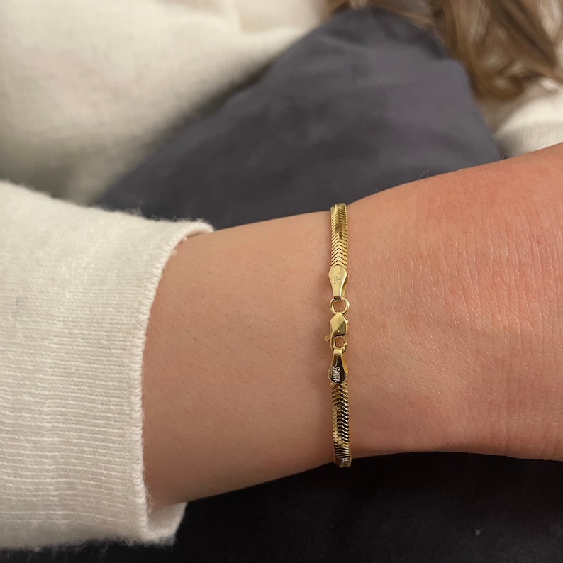 May include: A gold snake chain bracelet with a clasp that has the inscription "925".
