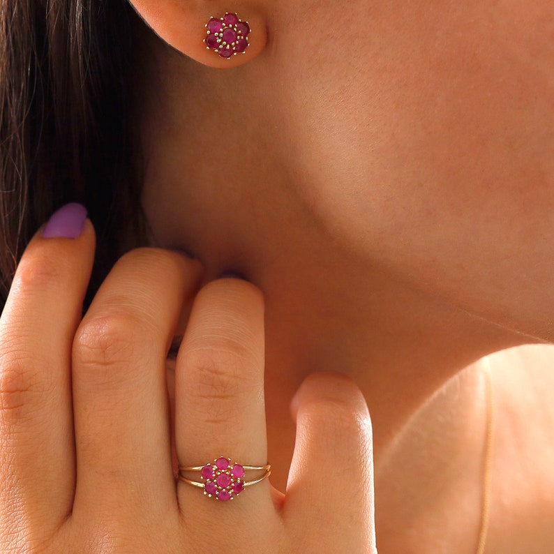 May include: A pair of gold earrings and a ring with a cluster of pink gemstones in the shape of a flower.