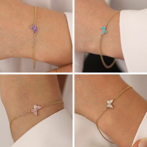 May include: Four gold chain bracelets with a butterfly charm. The butterflies are in different colors: purple, turquoise, pink, and white.