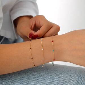 May include: Four gold chain bracelets with different colored beads. The bracelets feature black, white, red, and turquoise beads.