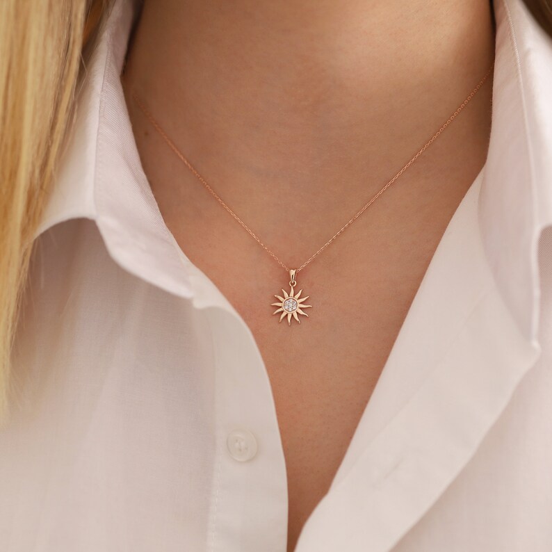 May include: A rose gold necklace with a small sun pendant featuring a clear crystal in the centre.