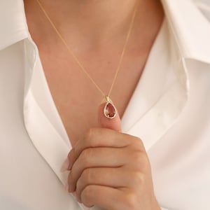 Pu&ograve; includere: Una collana con catena d'oro con un ciondolo a forma di pera con una pietra preziosa marrone circondata da pietre preziose trasparenti pi&ugrave; piccole.
