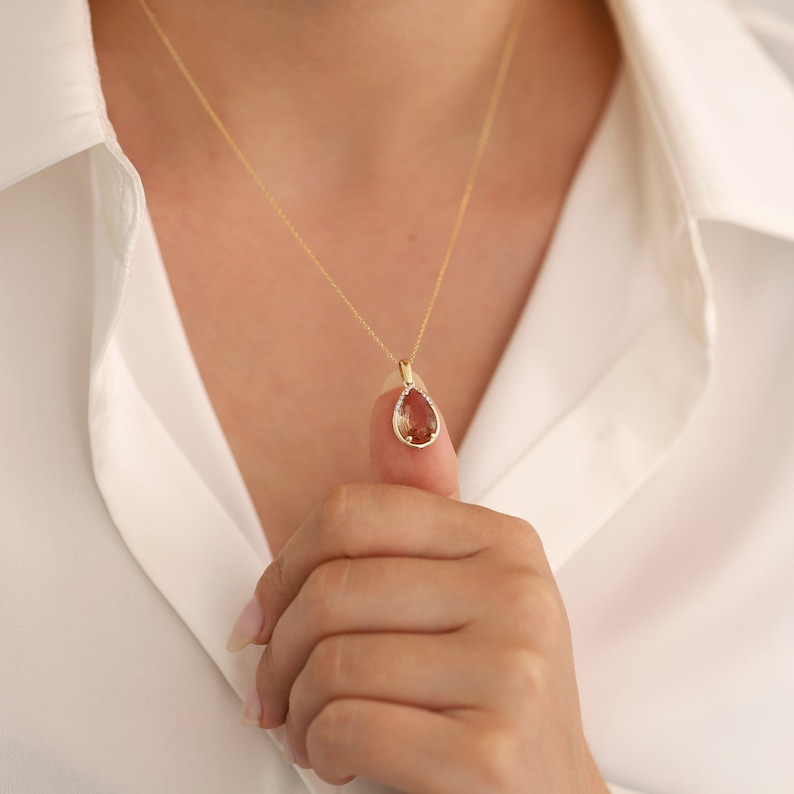 Pu&ograve; includere: Una collana con catena d'oro con un ciondolo a forma di pera con una pietra preziosa marrone circondata da pietre preziose trasparenti pi&ugrave; piccole.