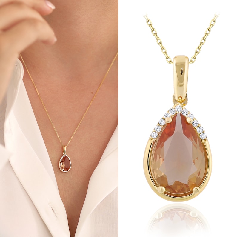 Pu&ograve; includere: Una collana d'oro con un ciondolo a forma di lacrima che presenta una pietra preziosa marrone circondata da piccole pietre preziose trasparenti.