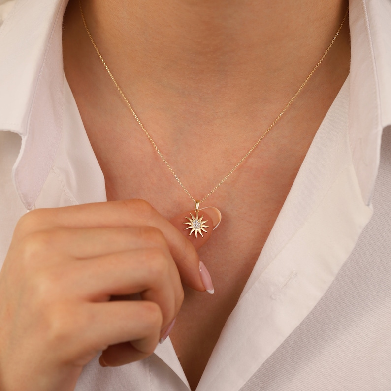 May include: A gold necklace with a heart-shaped pendant featuring a sun design with a small diamond in the centre.
