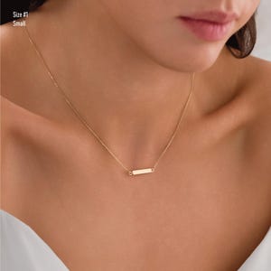 May include: A gold chain necklace with a small, rectangular pendant. The pendant is smooth and has a polished finish.