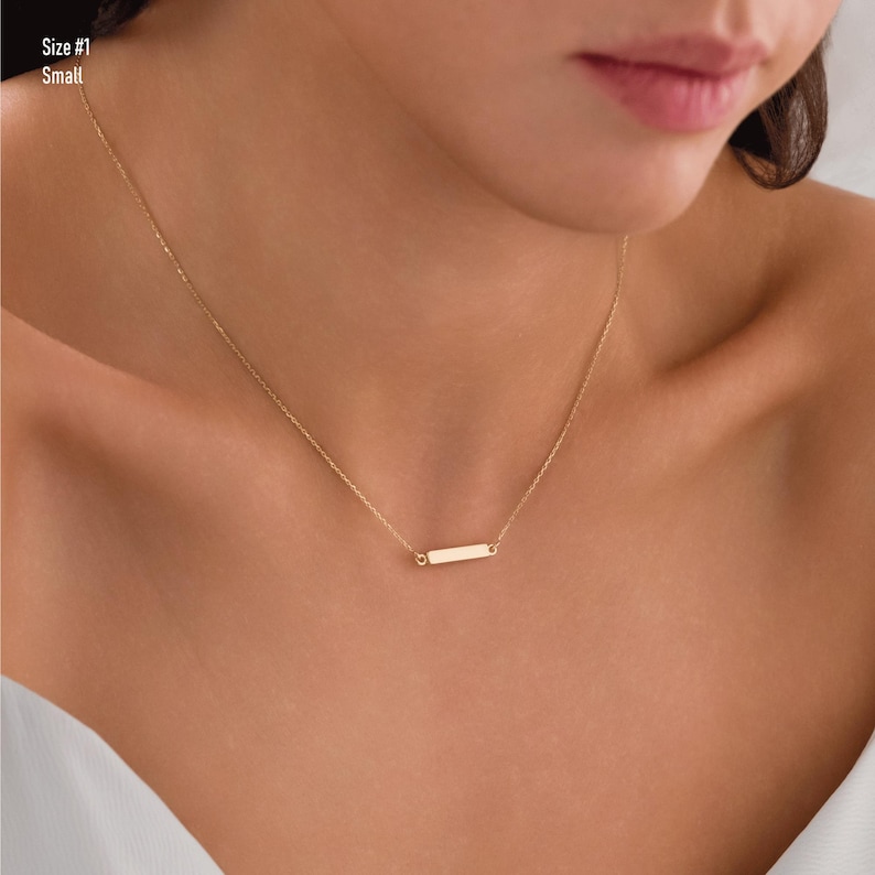 May include: A gold chain necklace with a small, rectangular pendant. The pendant is smooth and has a polished finish.