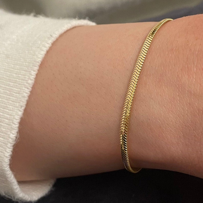 May include: A gold snake chain bracelet. The bracelet is thin and delicate, and it is made of a smooth, shiny metal.
