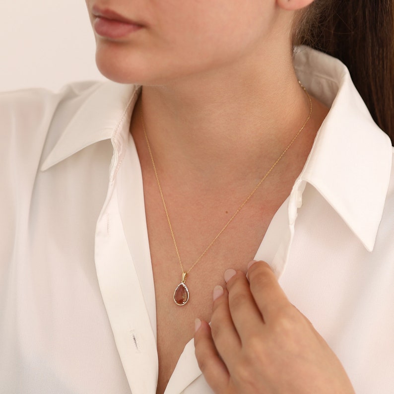 Pu&ograve; includere: Una collana con catena d'oro con un ciondolo a forma di lacrima che presenta una pietra preziosa marrone circondata da pietre preziose trasparenti pi&ugrave; piccole.