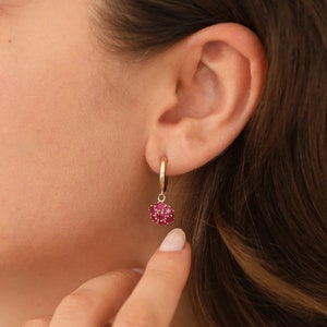 May include: Gold hoop earrings with a dangling cluster of red ruby stones.