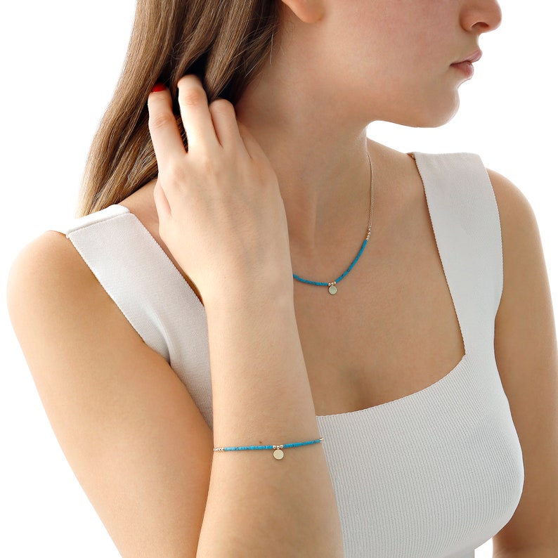 May include: A turquoise beaded necklace and bracelet with a gold disc pendant. The necklace and bracelet are both delicate and feminine.